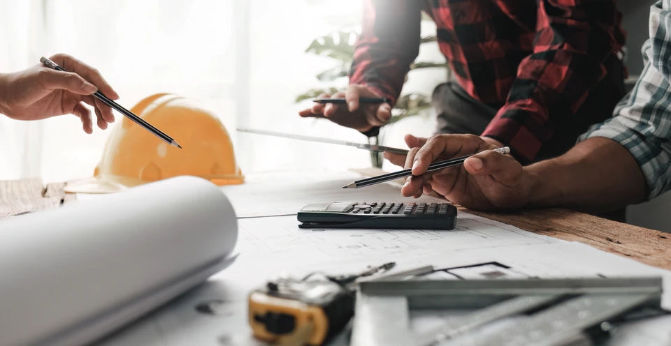 Deux professionnels du bâtiment analysent des plans d'architecture sur une table de travail