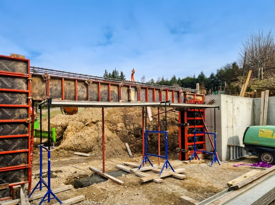 Chantier extérieur de construction d'un escalier en béton armé sur terrain en pente, entouré de conifères